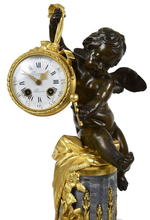 fig 1. A 19th-century French three-piece garniture set featuring a central patinated bronze cherub holding a clock atop a grey marble base, flanked by a pair of matching bronze cherub two-light candelabra.