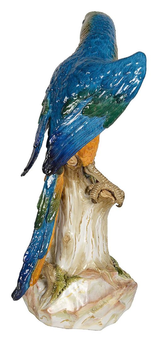 A polychrome porcelain figurine of a parrot with blue, green, and yellow feathers perched on a tree stump. View VI