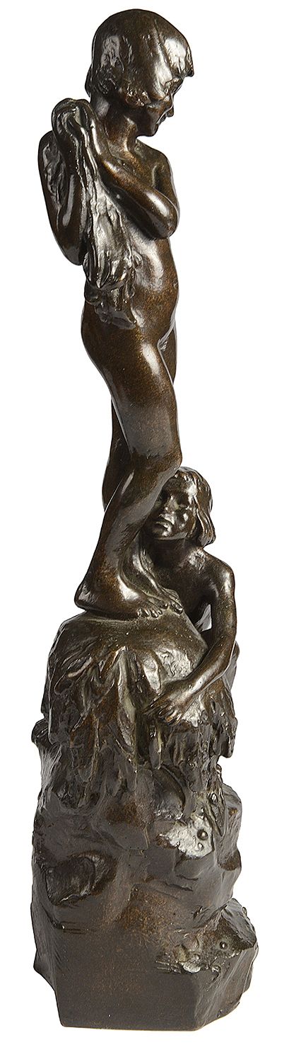 fig 2. A dark brown patinated bronze sculpture depicting two young children near a rock formation, with one standing above holding a towel and the other crouching at the base.