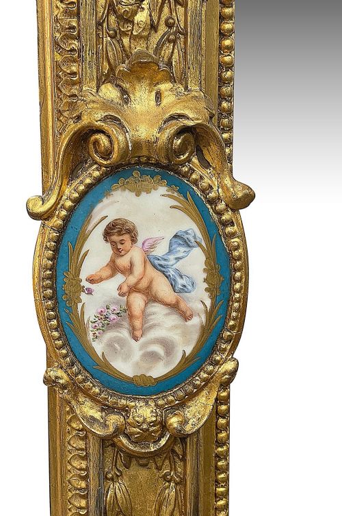 A large gilt-bronze wall mirror featuring an arched crest with sculpted putti, foliage mouldings, and oval Sevres porcelain plaques set along the frame. View VI