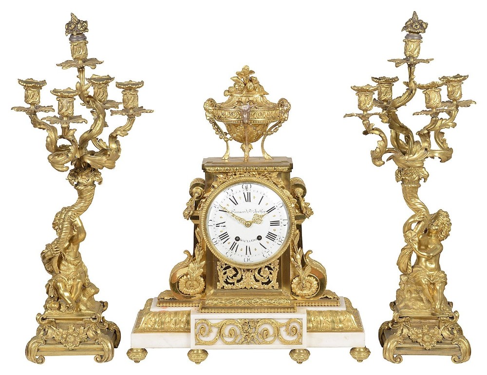A 19th-century French Louis XVI style gilt bronze clock garniture featuring a central urn-topped mantel clock flanked by two matching putti five-light candelabra.