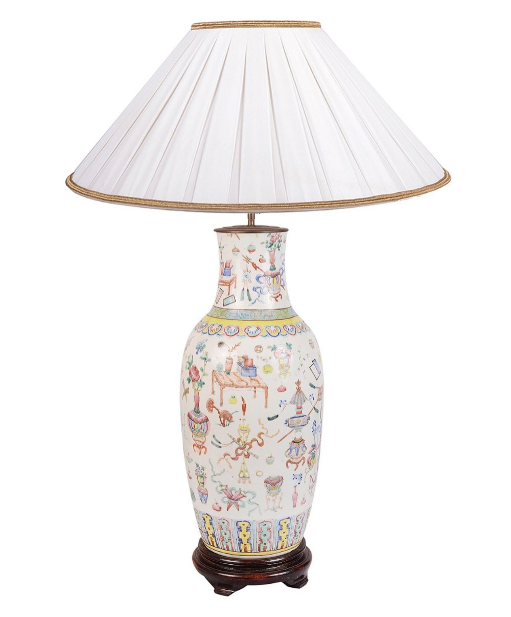 A 19th-century Chinese Famille Rose porcelain vase lamp featuring hand-painted precious objects on a cream background with a carved wooden base and pleated shade.