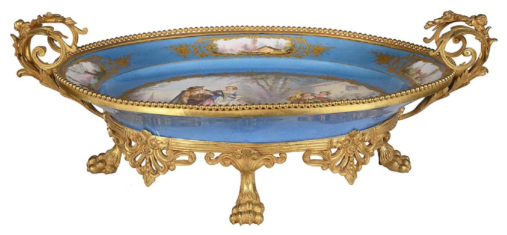 An oval sky-blue porcelain comport mounted in gilt bronze with twin scroll handles, lion paw feet, and hand-painted figurative reserves.