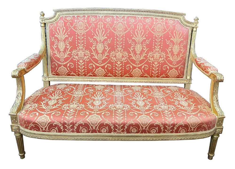 A French Louis XVI style two-seater settee featuring a carved gold-finish frame, fluted legs, and red Neoclassical pattern upholstery.