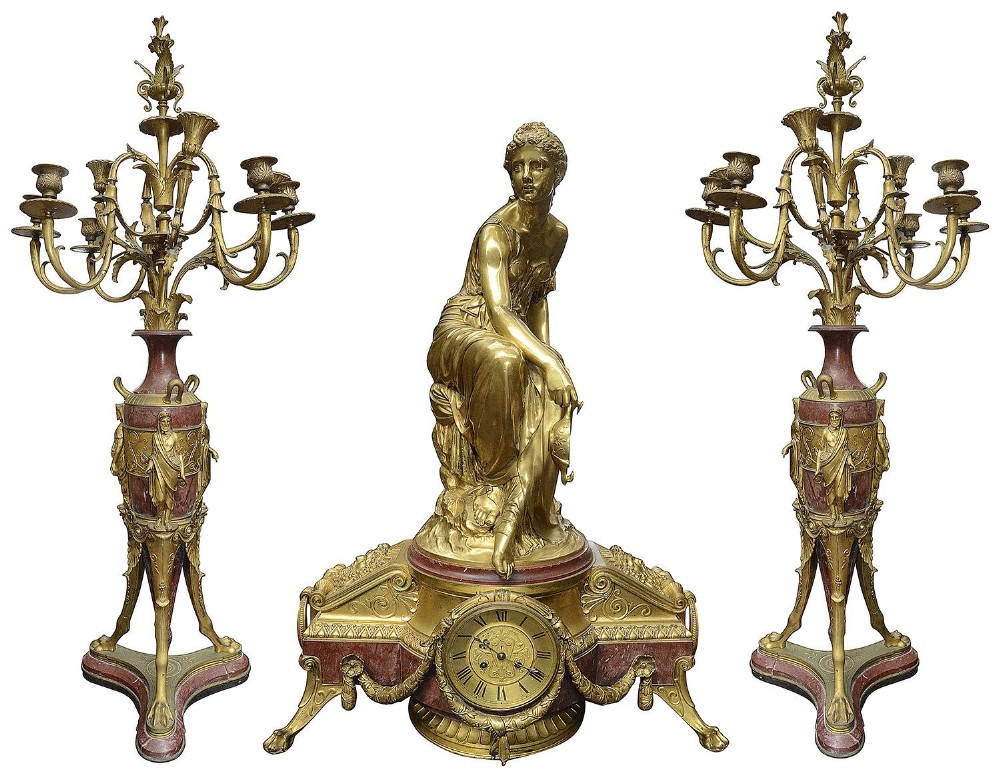 A three-piece Louis XVI style garniture set featuring a central gilt bronze classical female figure above a clock dial, flanked by two multi-light matching candelabra on red marble bases.