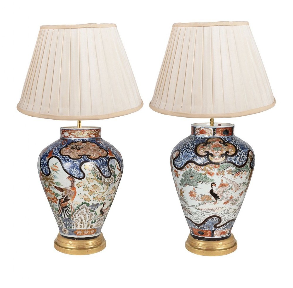 A pair of Japanese Imari porcelain vase table lamps with hand-painted bird and botanical motifs mounted on circular gilt bases with pleated cream shades.