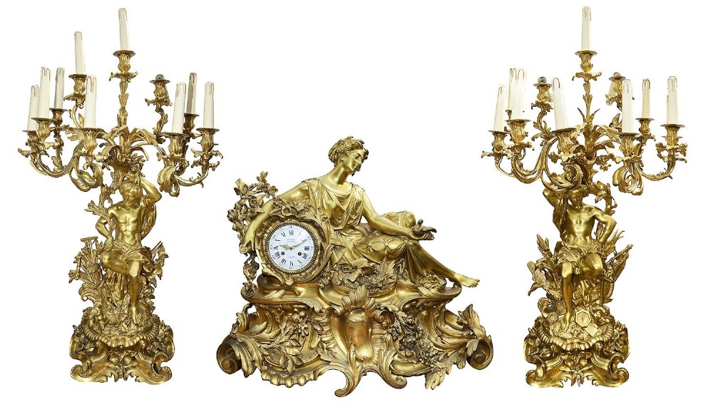 A nineteenth-century gilt bronze clock garniture set comprising a central reclining classical female figure beside a clock dial flanked by two multi-arm candelabra.
