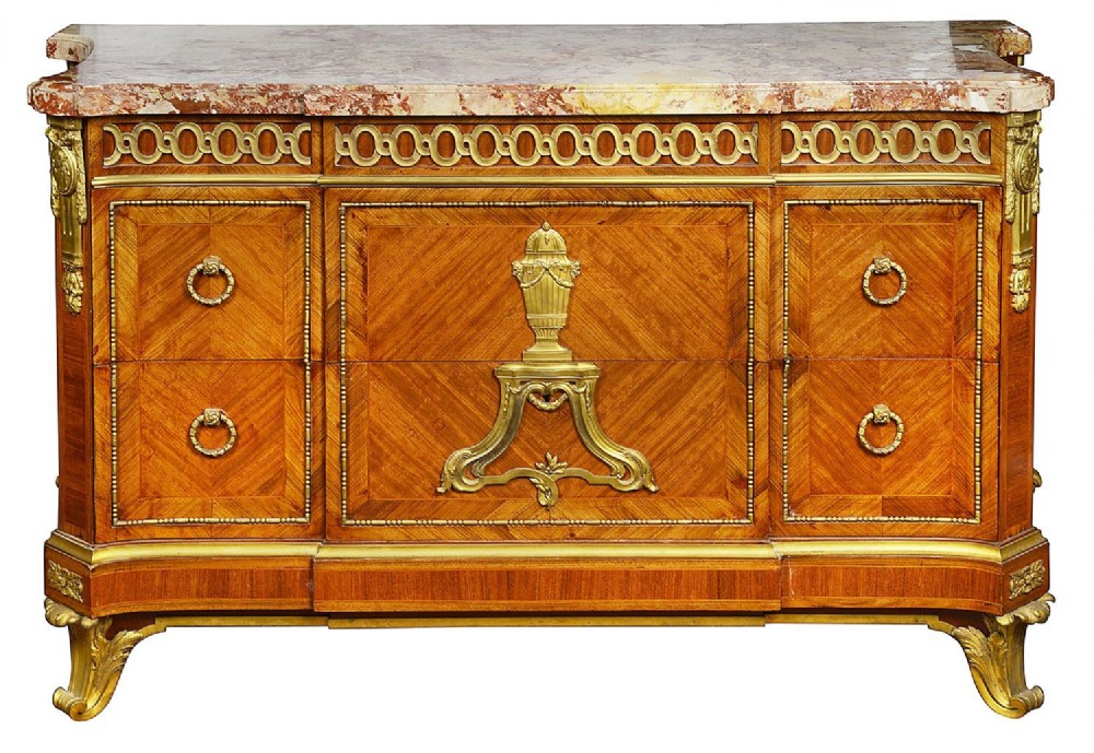 A nineteenth-century Louis XVI style wooden commode featuring parquetry veneering, gilt-bronze mounts, an urn motif, and a variegated marble top surface.