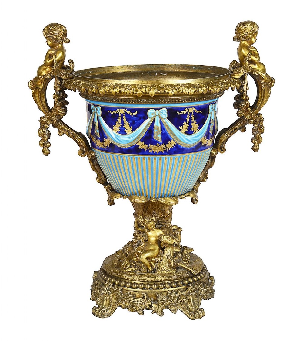 A 19th-century French porcelain urn with blue glazed decoration, ribbon swags, and gilt bronze mounts featuring cherub figures on the handles and base.
