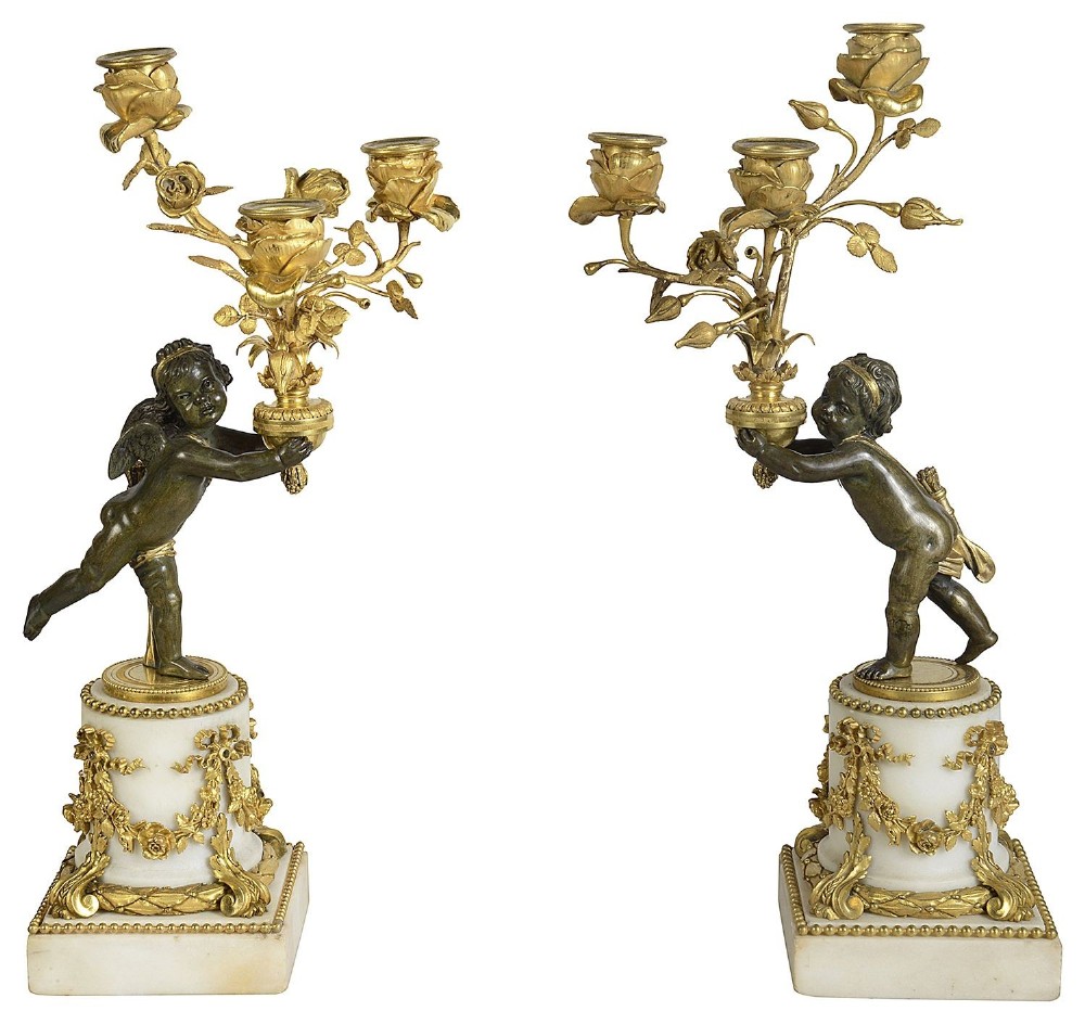A pair of nineteenth-century French candelabra featuring patinated bronze cherubs holding gilt bronze rose-form candle branches, mounted on white marble plinths adorned with gilt swags.