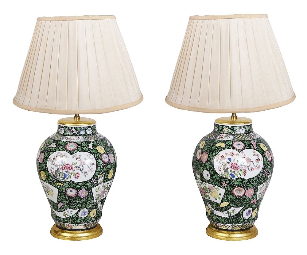 A pair of antique Chinese Famille Verte style ceramic vase lamps with black and green floral motifs and pleated cream shades.