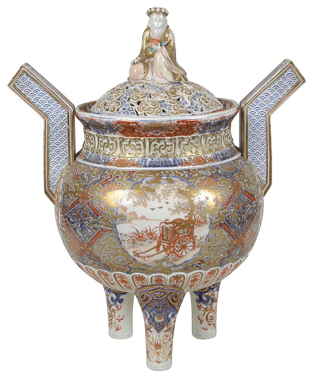 A Japanese Imari porcelain tripod koro featuring a pierced reticulated lid topped with a figural finial, angled side handles, and gold, blue, and rust-red hand-painted decoration.