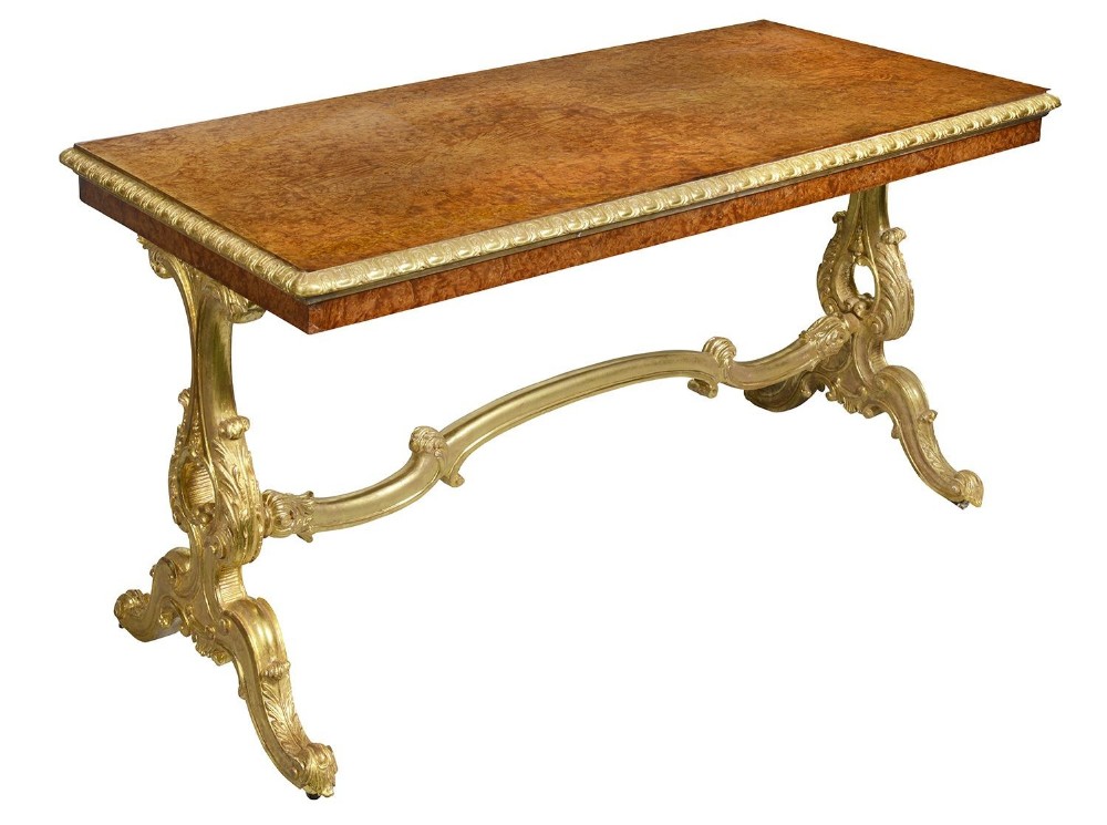 A Victorian centre table featuring a rectangular burr walnut top with gilded egg-and-dart moulding supported by carved giltwood scroll legs and a curved stretcher.