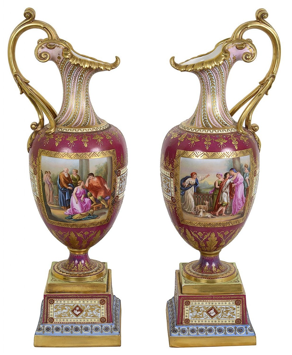 A pair of late nineteenth-century Vienna porcelain ewers featuring hand-painted classical panels, rich claret ground, gilded handles, and ornate square pedestal bases.
