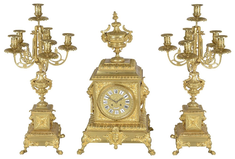 A 19th-century French gilt bronze clock garniture set comprising a central square clock topped with an urn, flanked by two matching multi-arm candelabras.
