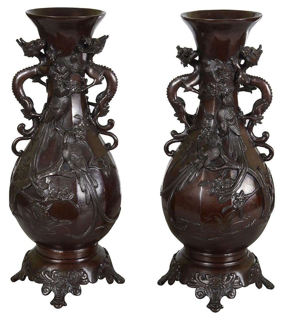 A pair of 19th-century Japanese dark brown bronze vases featuring relief carvings of birds on branches, dragon-formed handles, and elaborate scroll bases.