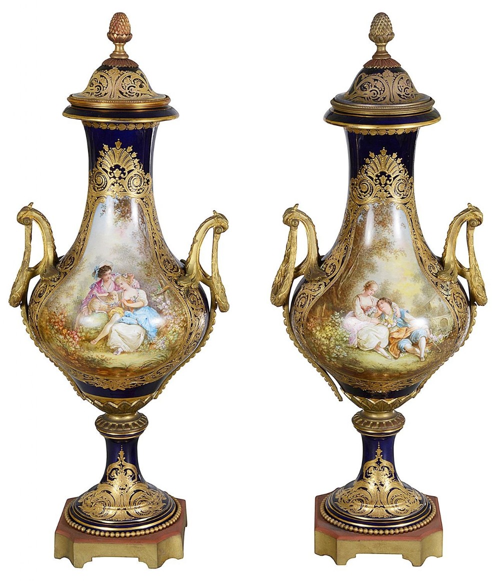 A pair of nineteenth-century Sevres style cobalt blue porcelain lidded vases featuring hand-painted romantic pastoral scenes, gilded scrollwork, twin handles, and finials.