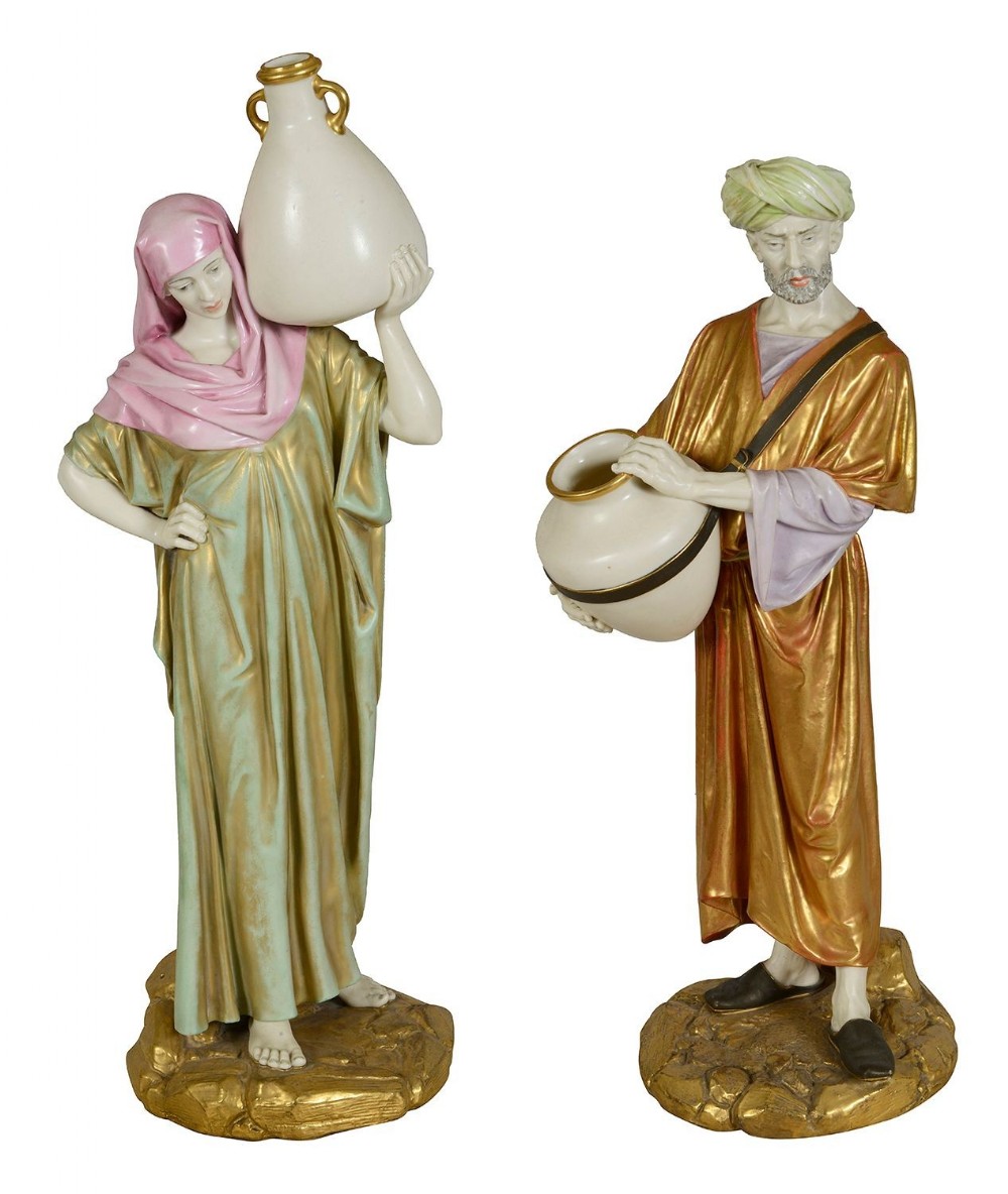 A pair of late nineteenth-century Worcester porcelain figures depicting a male and female Arab water carrier in draped robes holding ceramic jars.