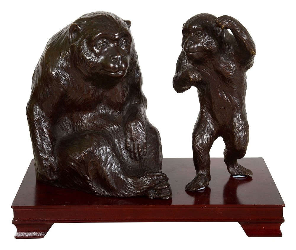A patinated dark bronze sculpture depicting a large seated monkey alongside a smaller standing monkey, both set on a polished rectangular wooden base.
