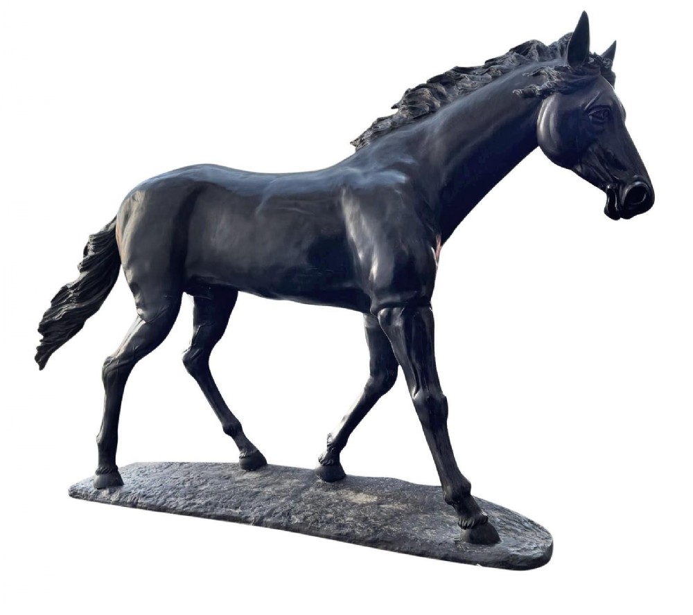 A life-size dark bronze statue of a stallion captured in motion standing on an integrated ground-style base.