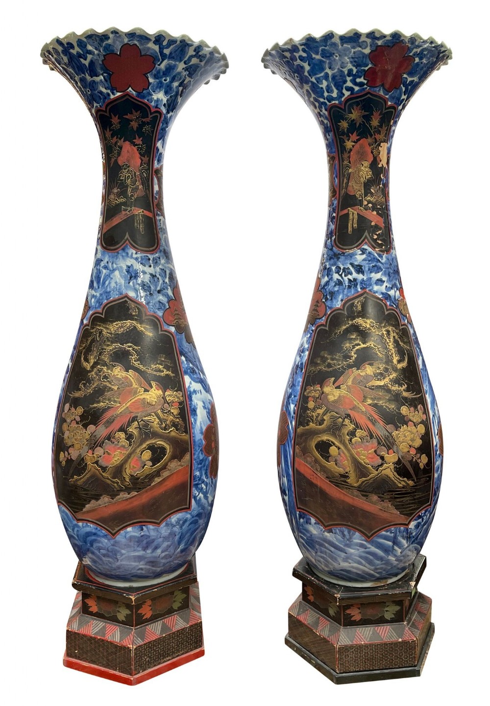 A pair of tall Japanese blue and white porcelain floor vases featuring black and gold lacquered panels depicting phoenixes, resting on carved wooden bases.
