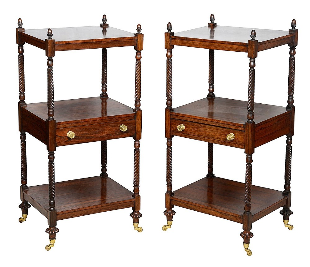 A pair of Regency rosewood three-tier what-nots featuring spiral-turned supports, corner finials, a central drawer with brass knobs, and brass castors.
