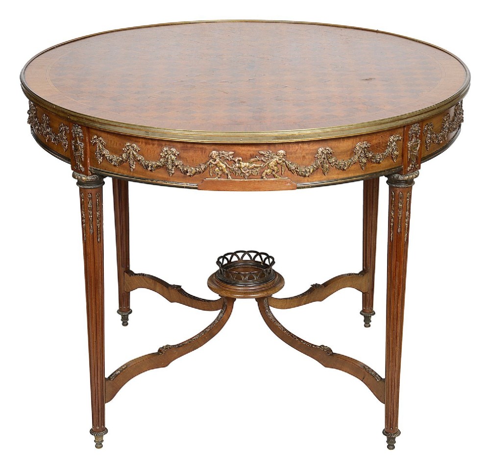 A circular late 19th-century French gueridon table featuring parquet wood marquetry, gilt-bronze frieze mounts depicting putti garlands, fluted legs, and a central stretcher gallery.