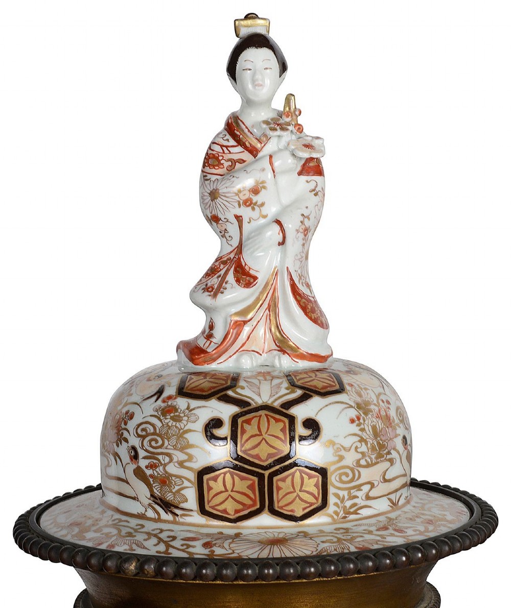 Pair of Japanese Arita Imari porcelain lidded vases featuring painted figures under umbrellas, standing on bronze bases with standing figure finials. View III