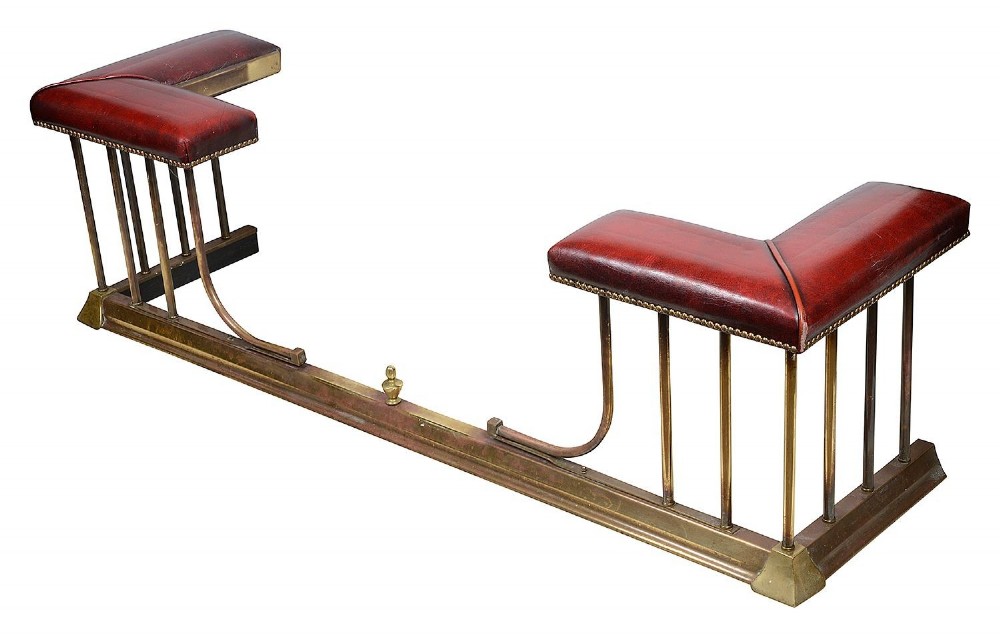 Late 19th-century brass club fender featuring twin red leather corner seats with stud trim and vertical brass spindles.