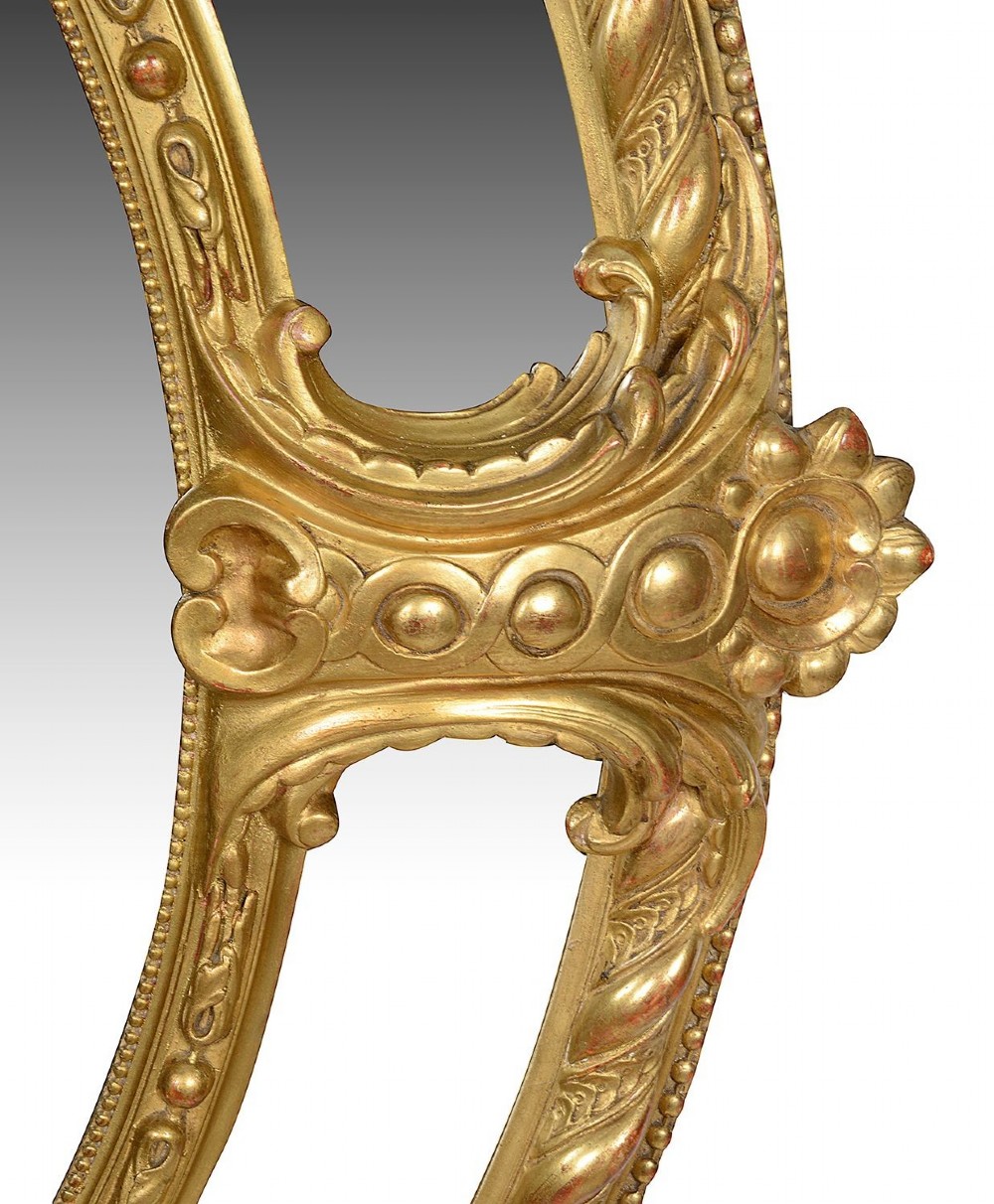 An ornate 19th-century oval wall mirror featuring a gilded wood and gesso frame with pierced scrollwork, shell cresting, and floral motifs. View IV