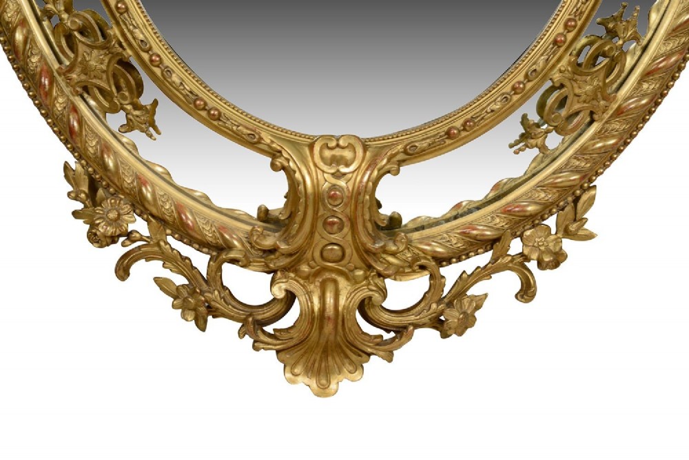 An ornate 19th-century oval wall mirror featuring a gilded wood and gesso frame with pierced scrollwork, shell cresting, and floral motifs. View VI