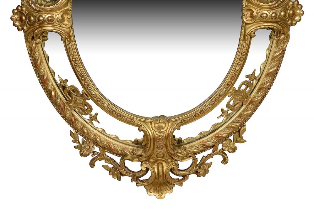 An ornate 19th-century oval wall mirror featuring a gilded wood and gesso frame with pierced scrollwork, shell cresting, and floral motifs. View VII