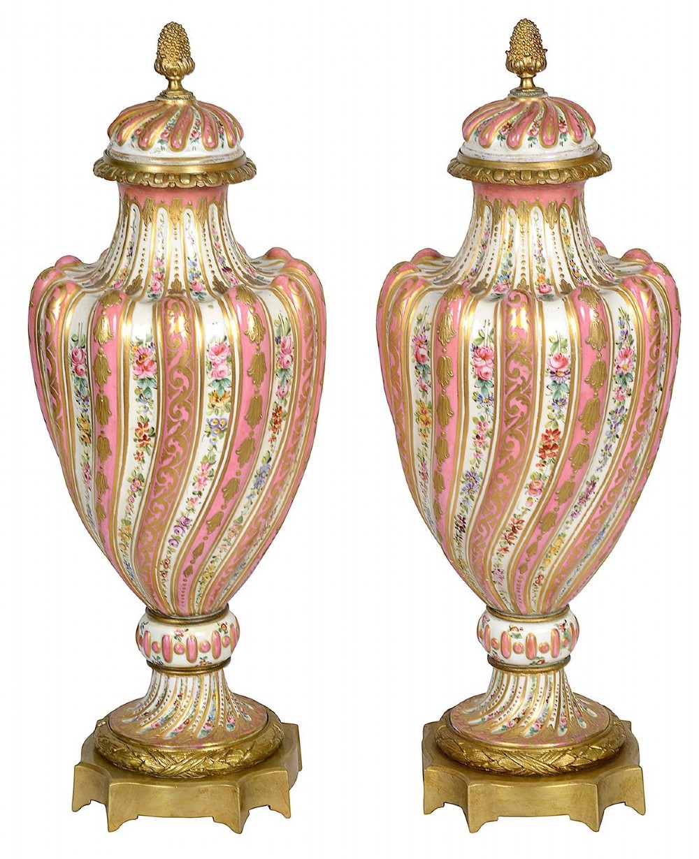 A pair of 19th-century French Sevres style pink and white porcelain lidded vases featuring hand-painted floral stripes and gilt decoration on square bases.