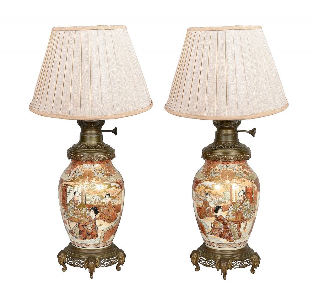 A pair of 19th-century Japanese Satsuma porcelain table lamps with brass mounts, elephant-head tripod bases, and pleated cream silk lampshades.