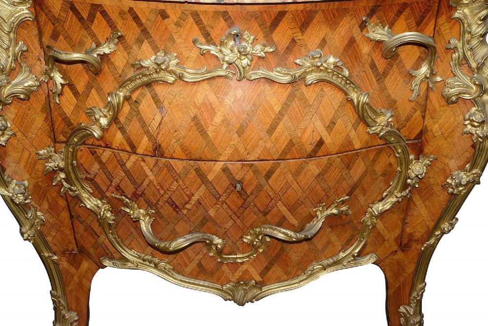 A pair of French eighteenth-century style bombe commodes with geometric wood parquetry, intricate gilt-bronze mounts, and variegated marble tops. View V