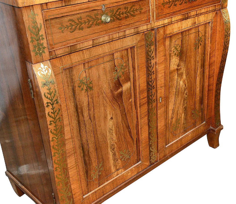 A Regency period warm brown timber chiffonier featuring intricate brass scrollwork inlay, a raised shelf gallery with two small drawers, and a two-door lower cabinet. View IV