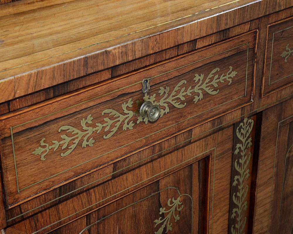 A Regency period warm brown timber chiffonier featuring intricate brass scrollwork inlay, a raised shelf gallery with two small drawers, and a two-door lower cabinet. View IX