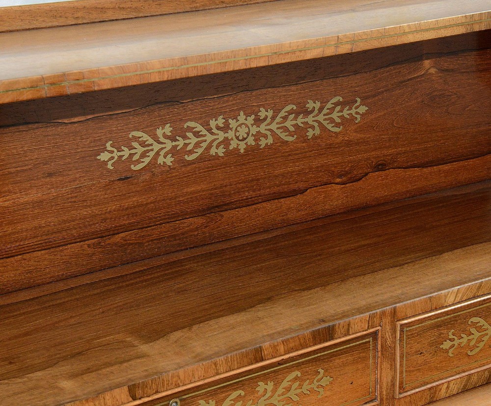 A Regency period warm brown timber chiffonier featuring intricate brass scrollwork inlay, a raised shelf gallery with two small drawers, and a two-door lower cabinet. View X