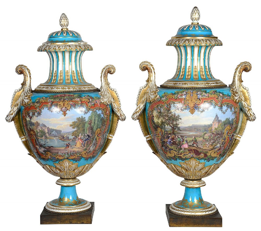 A pair of turquoise blue Sevres-style porcelain urns featuring hand-painted pastoral scenes, gilded scroll handles, and pineapple finials on square metal bases.