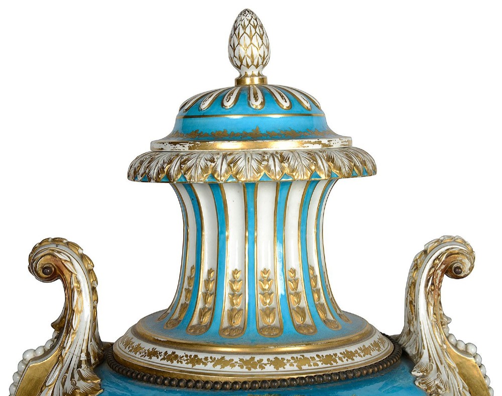 A pair of turquoise blue Sevres-style porcelain urns featuring hand-painted pastoral scenes, gilded scroll handles, and pineapple finials on square metal bases. View IV