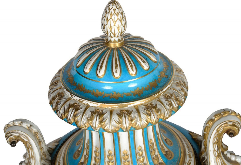 A pair of turquoise blue Sevres-style porcelain urns featuring hand-painted pastoral scenes, gilded scroll handles, and pineapple finials on square metal bases. View V