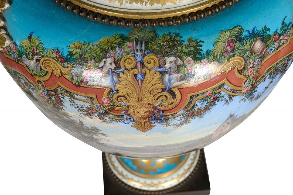 A pair of turquoise blue Sevres-style porcelain urns featuring hand-painted pastoral scenes, gilded scroll handles, and pineapple finials on square metal bases. View IX