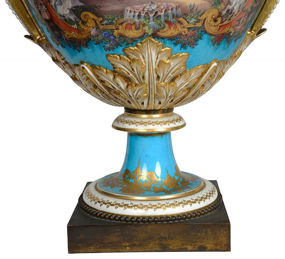 A pair of turquoise blue Sevres-style porcelain urns featuring hand-painted pastoral scenes, gilded scroll handles, and pineapple finials on square metal bases. View XV