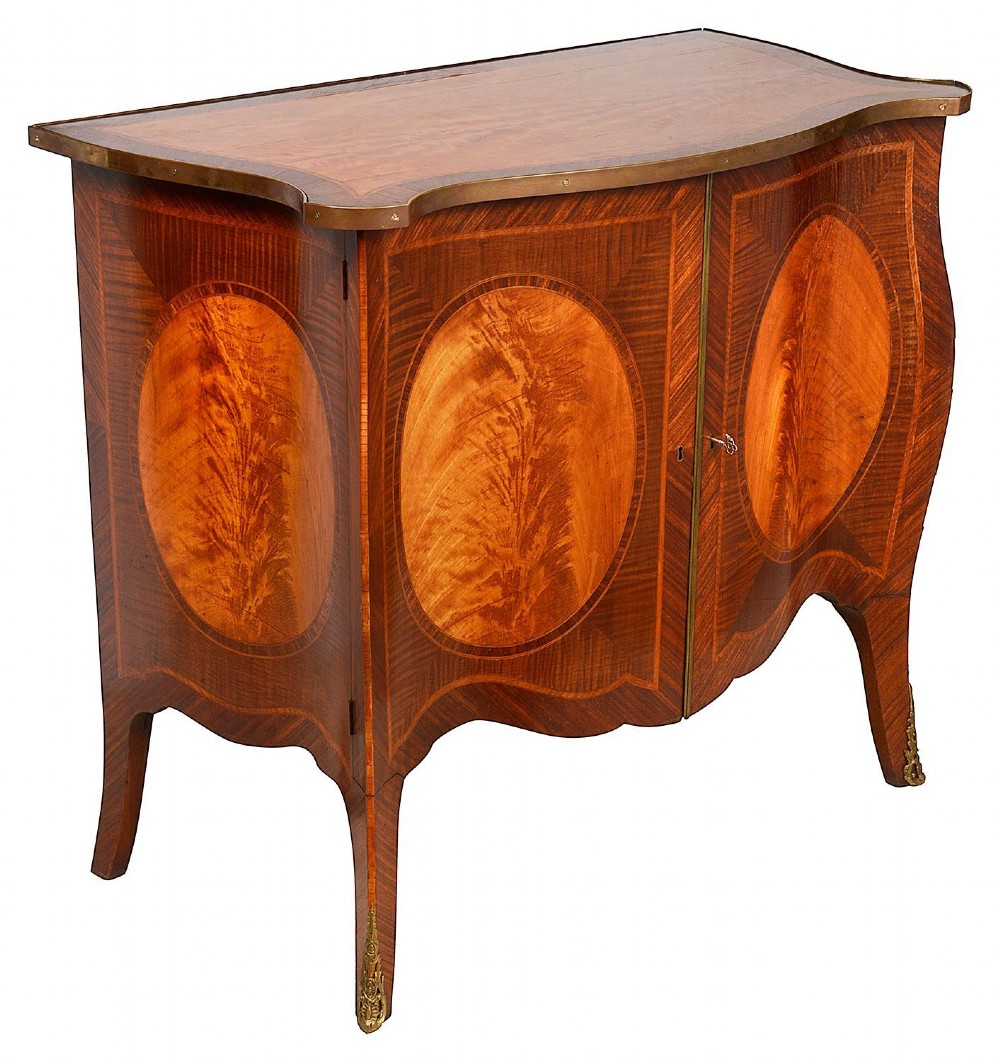 A pair of early 20th-century serpentine mahogany and satinwood commodes with oval central inlays and brass feet. View IV