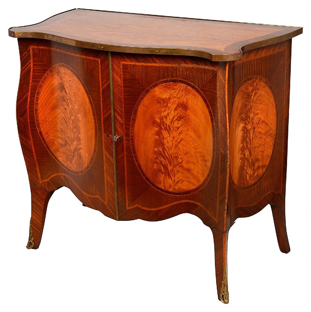 A pair of early 20th-century serpentine mahogany and satinwood commodes with oval central inlays and brass feet. View VI