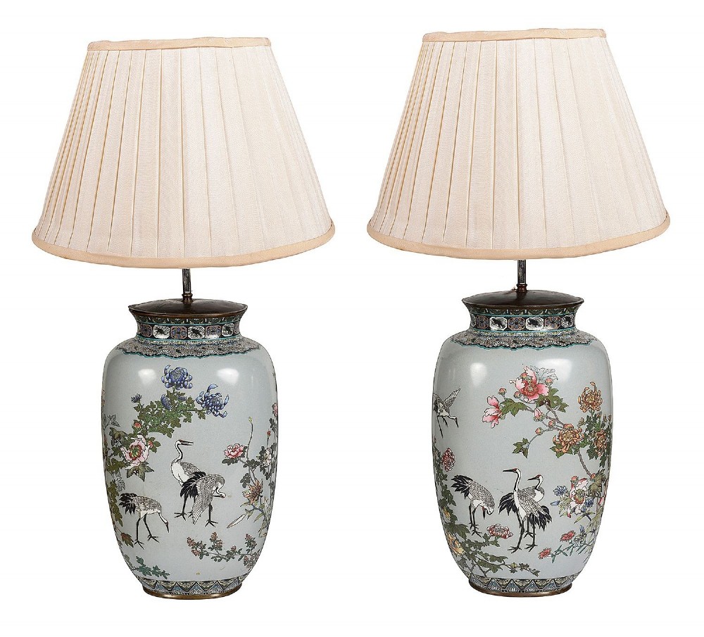 A pair of Japanese cloisonne enamel vase table lamps decorated with cranes and floral motifs on a light blue ground with cream pleated shades.