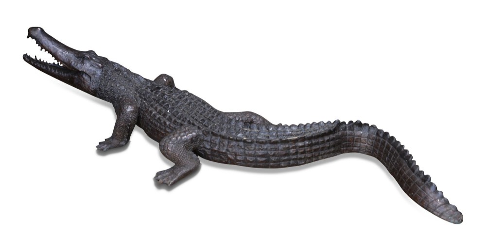 A life-size dark bronze sculpture of a crocodile depicted with open jaws, detailed scaly texture, and a curved tail.