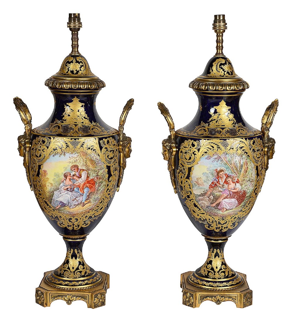 A pair of 19th-century French Sevres-style cobalt blue porcelain urn lamps featuring hand-painted romantic scenes, ornate gilt bronze mounts, and fringed fabric shades. View II