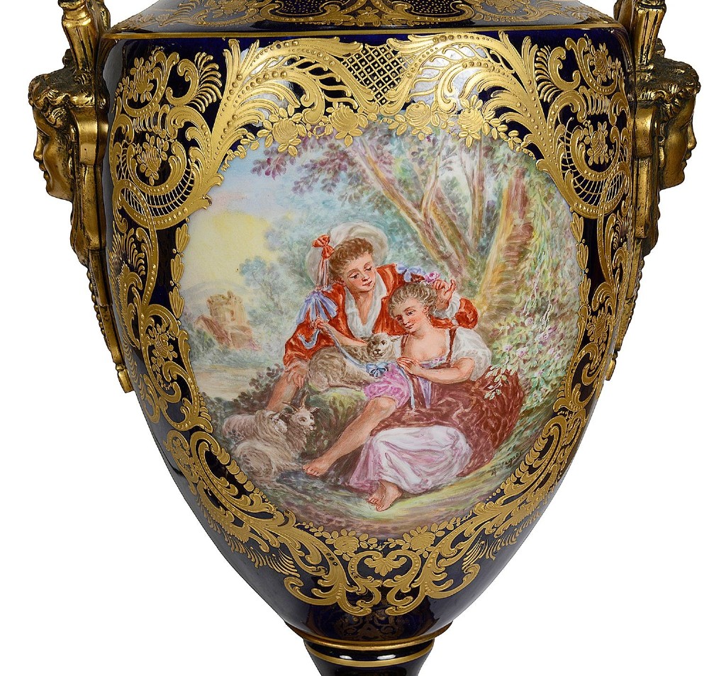 A pair of 19th-century French Sevres-style cobalt blue porcelain urn lamps featuring hand-painted romantic scenes, ornate gilt bronze mounts, and fringed fabric shades. View V