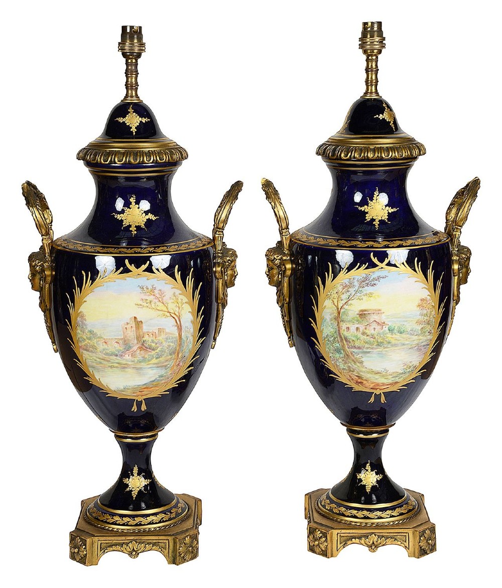 A pair of 19th-century French Sevres-style cobalt blue porcelain urn lamps featuring hand-painted romantic scenes, ornate gilt bronze mounts, and fringed fabric shades. View IX